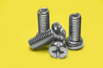 Close-up of metal chrome screws on yellow background