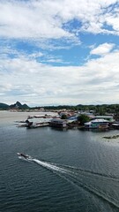 Scenic view of a tranquil water village with wooden houses and lush green hills under a blue sky with fluffy clouds, perfect for travel and nature themes © Nut S.