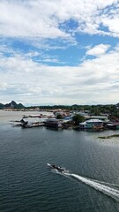 Serene Coastal Scene with Traditional Wooden Houses and Small Boat Navigating Calm Water Under Bright Blue Sky
