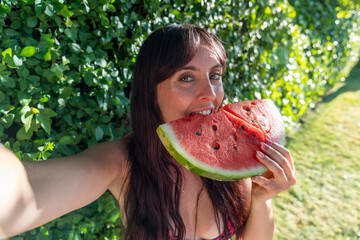 Happy brunette woman taking a selfie while eating watermelon in summer