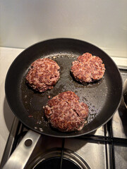 Three hamburger patty cooking on the pan.