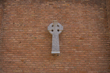 Stone Celtic cross mounted on a red brick wall