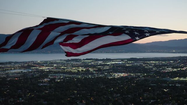 Massive, majestic American flag flowing over valley lights at dusk - drone shot