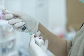 Doctor filling syringe with medication from vial on blurred background.