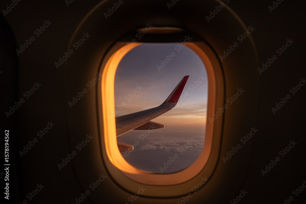 Wall mural view through window of wing of plane in colorful cloudscape while flying high against sky in sunset.
