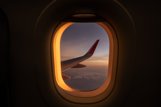 View through window of wing of plane in colorful cloudscape while flying high against sky in sunset.