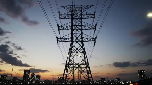 Silhouette Of Power Transmission Tower Over City At Dusk With Dramatic Purple and Orange Sky Gradient Cloud Background