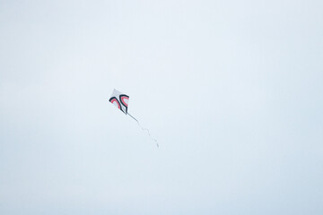 White kite with red and black abstract design flying alone against gradient light-blue and white sky background. Outdoor recreation concept