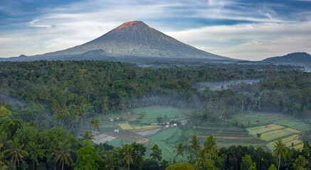 Mount Agung towers over lush forests and rice paddies in Abang, Bali, Indonesia. The volcano is a sacred site for the Balinese people, who visit to offer prayers and seek blessings.