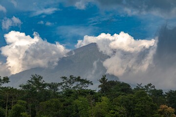 Mt Agung, an active volcano, rises above lush green trees and is partially obscured by clouds in...