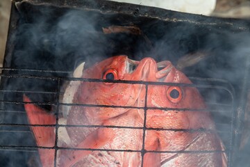 Freshly caught red snapper fish are grilled over an open fire in Ujung, Bali, Indonesia. The fish...