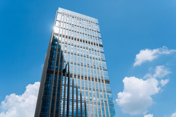 A modern glass office building reflecting the blue sky and white clouds, creating a sleek and...