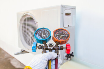 Air repair mechanic using measuring equipment for filling industrial factory air conditioners.	