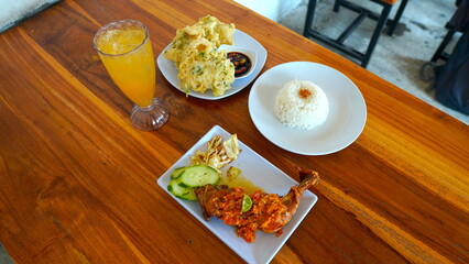 Delicious Indonesian Meal of Fried Chicken, Rice, and Vegetables on a Wooden Table