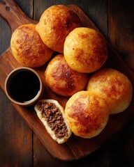 Golden-brown savory pastries on a wooden board with a small bowl of dipping sauce nearby