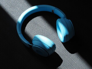 Blue headphones are placed on yoga mat surface. Light streams across them.