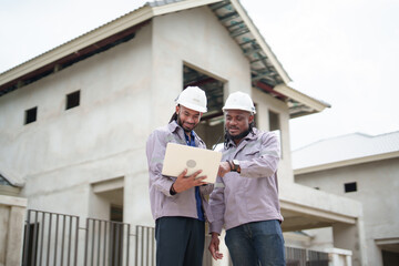 Two African male engineers wearing helmets and uniform using laptop for project planning and...