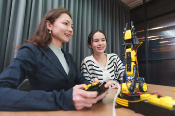 Caucasian woman teacher helps Asian girl learn robotics and teamwork in a modern STEM classroom.