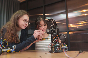 Teacher helps Asian girl student teamwork to build robotics arm and STEM hands-on.