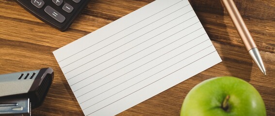 Paper by stapler and calculator with apple on table