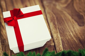 Flat design white gift box is sitting on wooden tabletop, with red ribbon bow, pine branches
