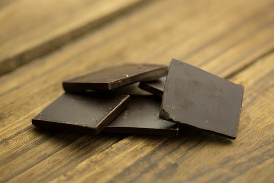Naklejki Dark chocolate squares are being stacked on rustic wooden tabletop, highlighting glossy surfaces