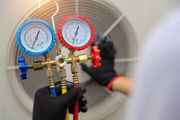 Air conditioning electrical technician using manifold gauge measuring tool checking refrigerant pump filling home air conditioner and maintenance heat fix repair and clean outdoor compressor unit.