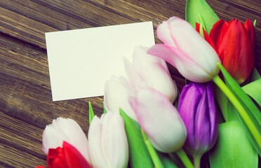 Flat design is featuring blank white card on rustic wooden tabletop with bright tulips lying beside