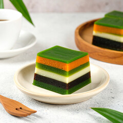 Traditional Indonesian kue lapis slice with natural gradient colors on clean beige ceramic plate
