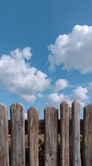 Rustic wooden fence under blue sky with fluffy clouds