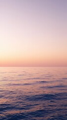 Obraz premium Soft sunset hues paint the sky above a serene ocean view with gentle ripples across the water's surface
