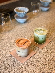 Iced matcha latte and iced coffee latte served in clear glasses on a textured countertop, perfect for a cozy café vibe and refreshing afternoon treat.