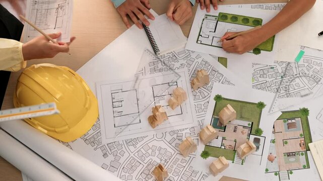 Architect and safety engineer discussion about building construction use blueprint on table with architectural document, measurement tool and wooden block scatter around at modern office. Delineation.