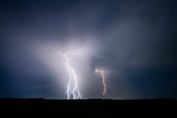 A strong storm is approaching with fierce bolts of lightning illuminate ominous clouds.