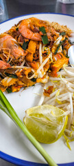 Pad Thai with fresh shrimp in a white plate with blue edges on a stainless steel table.