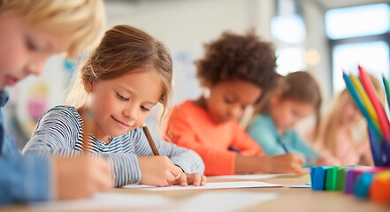 Diverse group of young elementary school children focused on drawing and writing at their desks in a bright classroom setting