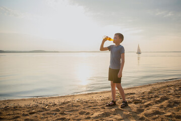 A boy, a child drinking a drink from a glass bottle, with a backdrop of the sea and a sailing ship...