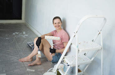Young woman painting indoors wall with roller using stepladder