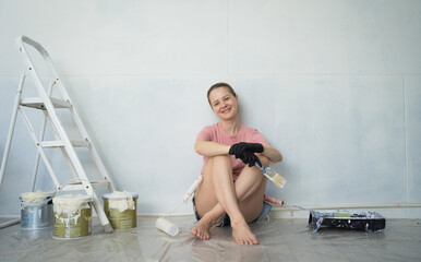 Young woman painting indoors wall with roller using stepladder