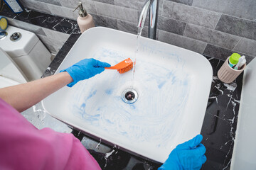 Young housewife diligently scrubs and cleans the sink in bathroom
