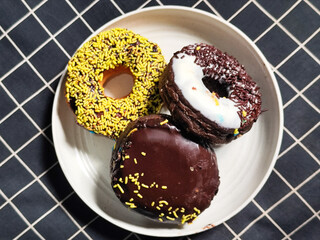Three delicious donuts topped with sprinkles and various colored glazes, displaying a tempting...