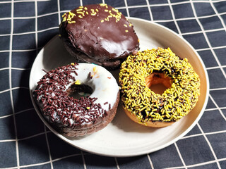 Three delicious donuts topped with sprinkles and various colored glazes, displaying a tempting...