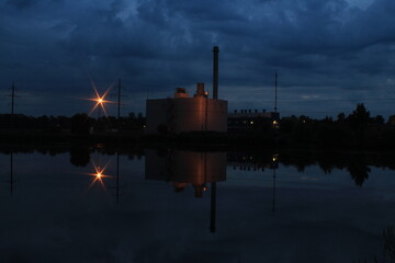 Industrial building with beautiful lighting brightly reflected in the water of the lake at dusk.