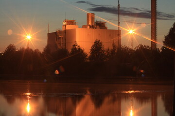 Industrial building with beautiful lighting brightly reflected in the water of the lake at dusk.