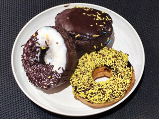Three delicious donuts topped with sprinkles and various colored glazes, displaying a tempting...