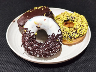 Three delicious donuts topped with sprinkles and various colored glazes, displaying a tempting...