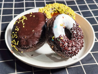 Three delicious donuts topped with sprinkles and various colored glazes, displaying a tempting...