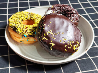 Three delicious donuts topped with sprinkles and various colored glazes, displaying a tempting...