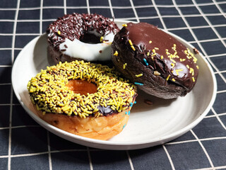 Three delicious donuts topped with sprinkles and various colored glazes, displaying a tempting...
