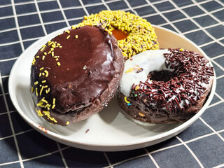 Three delicious donuts topped with sprinkles and various colored glazes, displaying a tempting...